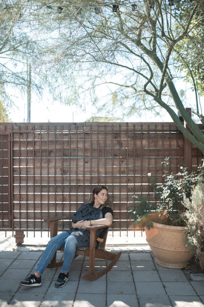 pexels-photo-6849462 A woman relaxes outdoors on a wooden rocking chair under a tree, enjoying a sunny day.